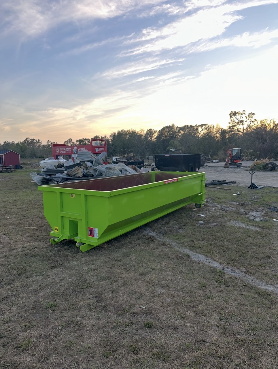 Green Madd Dumpsters roll off container placed on a property at sunset